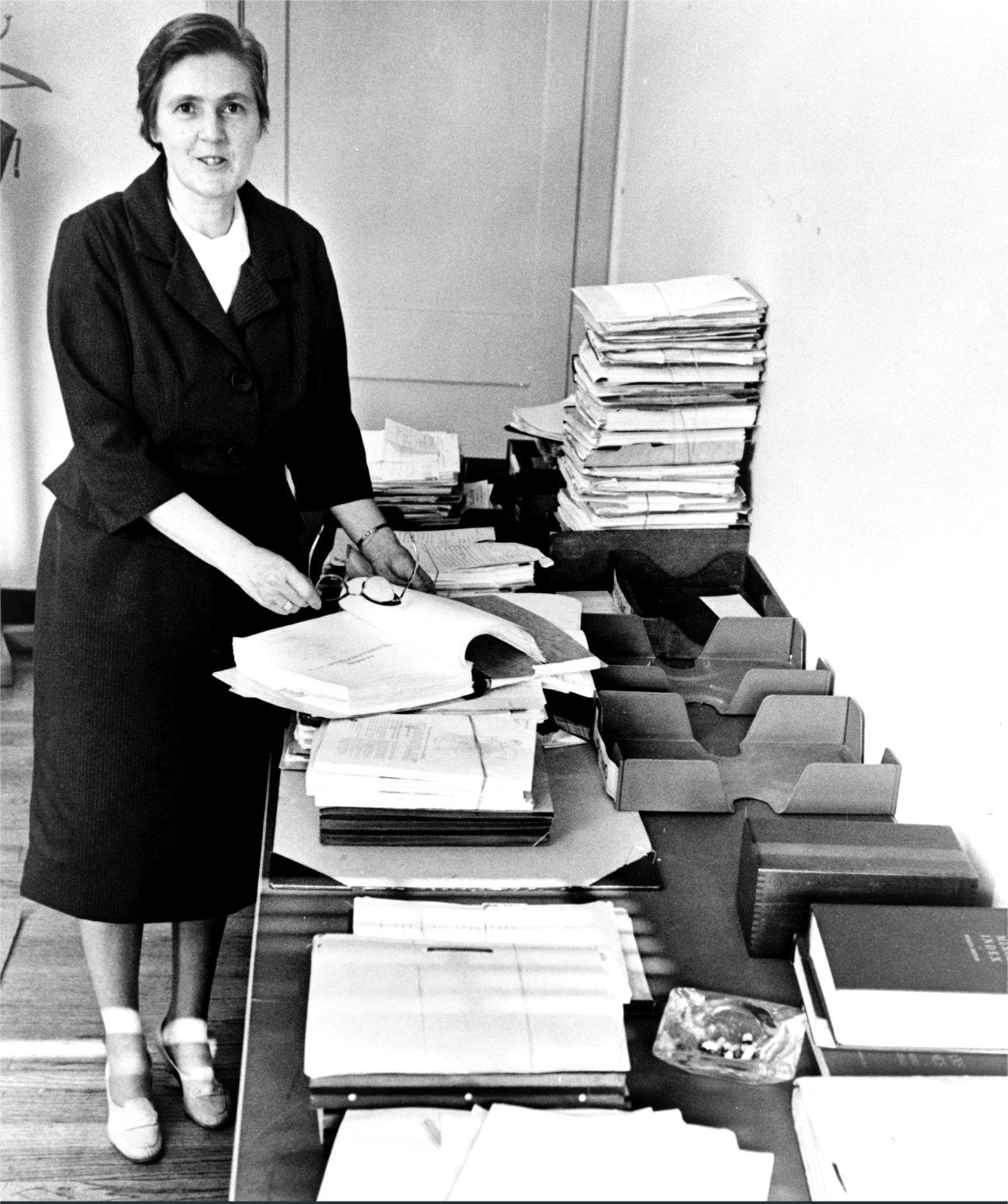 Frances Kelsey at her FDA desk with stacks of drug application files, 1960s